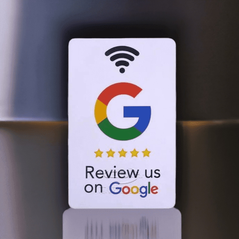 A google review card featuring the Google logo and "Review us on Google" text with a row of five golden stars. Above the logo is a stylized Wi-Fi symbol. The background showcases blurred gray and brown hues, ideal for an NFC station display.