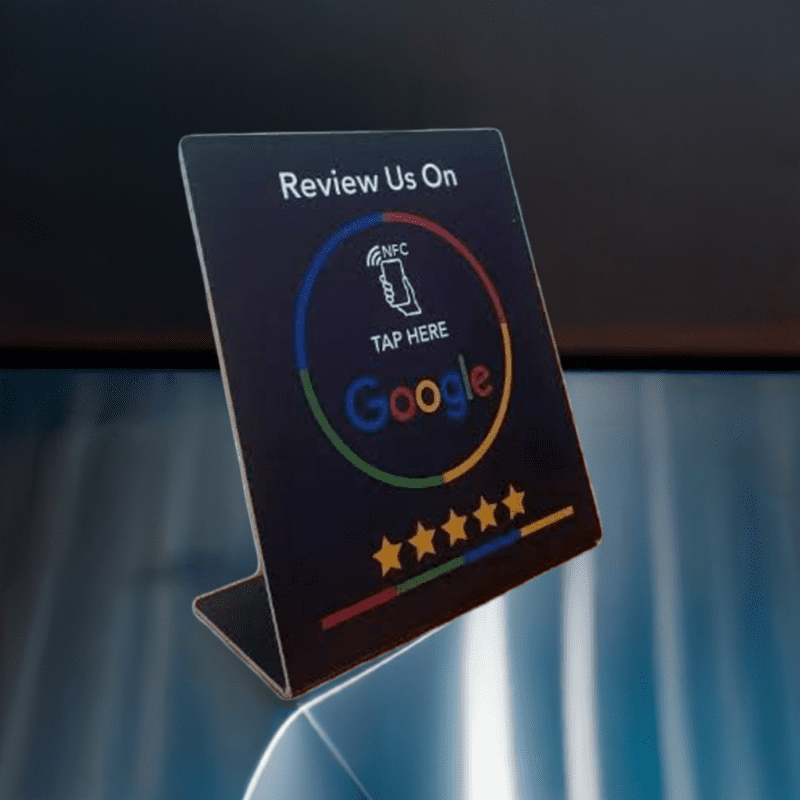 A small Google Review Card NFC Station (Black) is shown with a "Tap Here" icon indicating an NFC feature. The stand encourages users to review the service on Google and has a row of five stars at the bottom, suggesting a rating system.