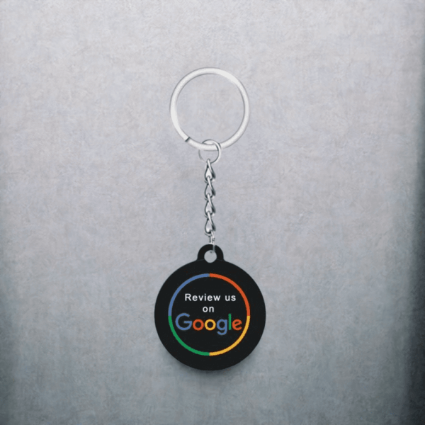 A keychain with a black circular tag hangs against a gray background. The tag features the Google logo and colorful text saying "Review us on Google." This sleek NFC keychain for Google reviews makes it easy for customers to leave feedback with just a tap.